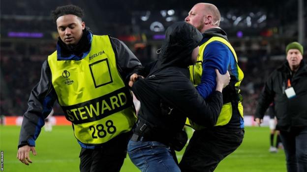 Un envahisseur de terrain escorté hors du terrain par des stewards lors du match PSV contre Séville