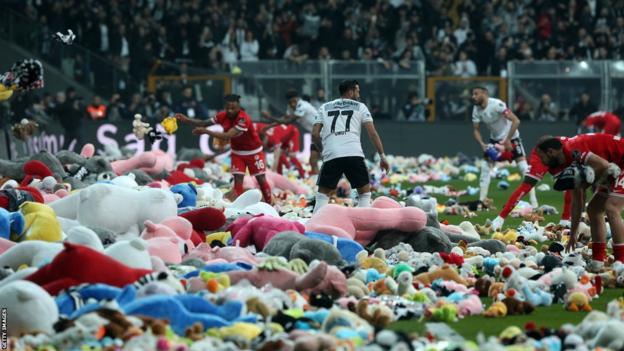 Les joueurs retirent les ours en peluche du terrain, jetés sur le terrain en soutien aux enfants victimes du tremblement de terre